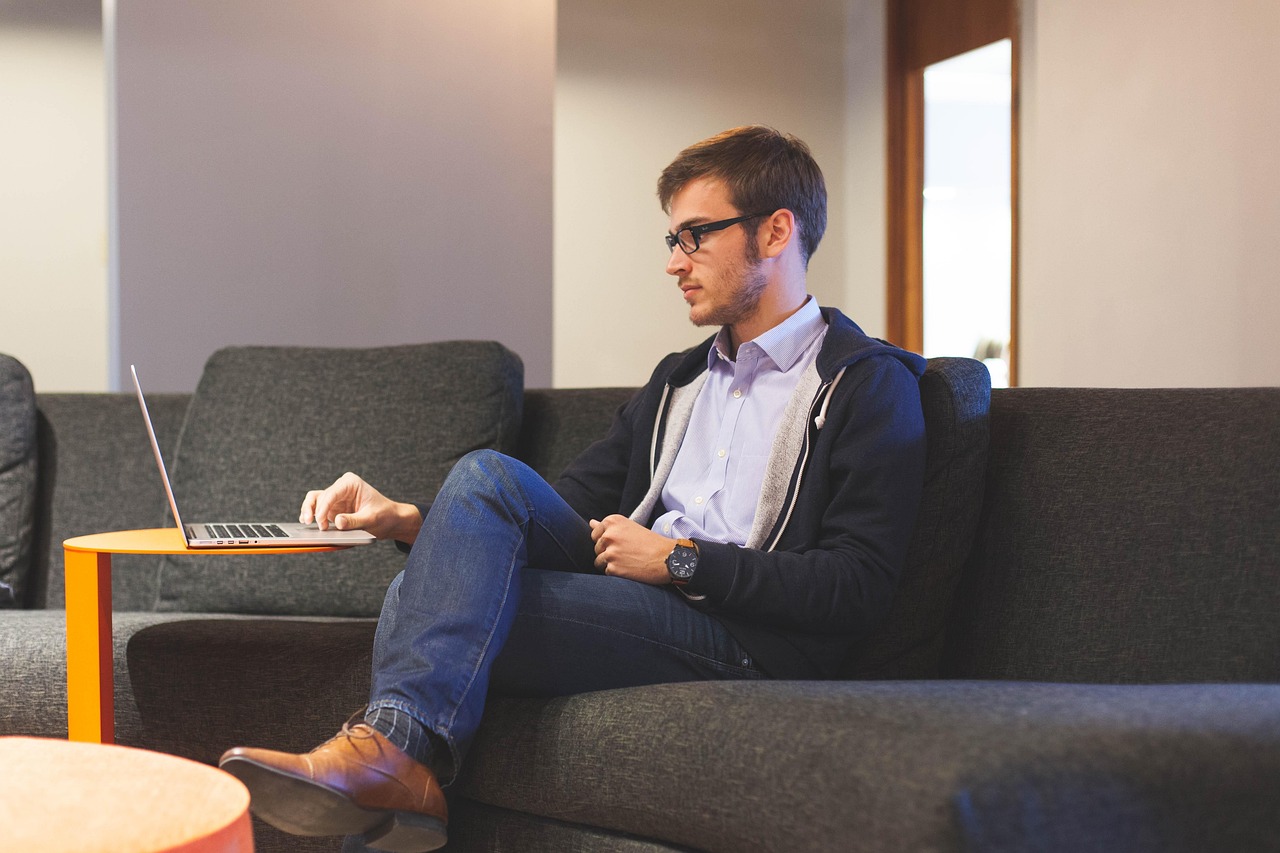 Man sitting on a couch working on a laptop, representing an entrepreneur leveraging AI in recruitment.